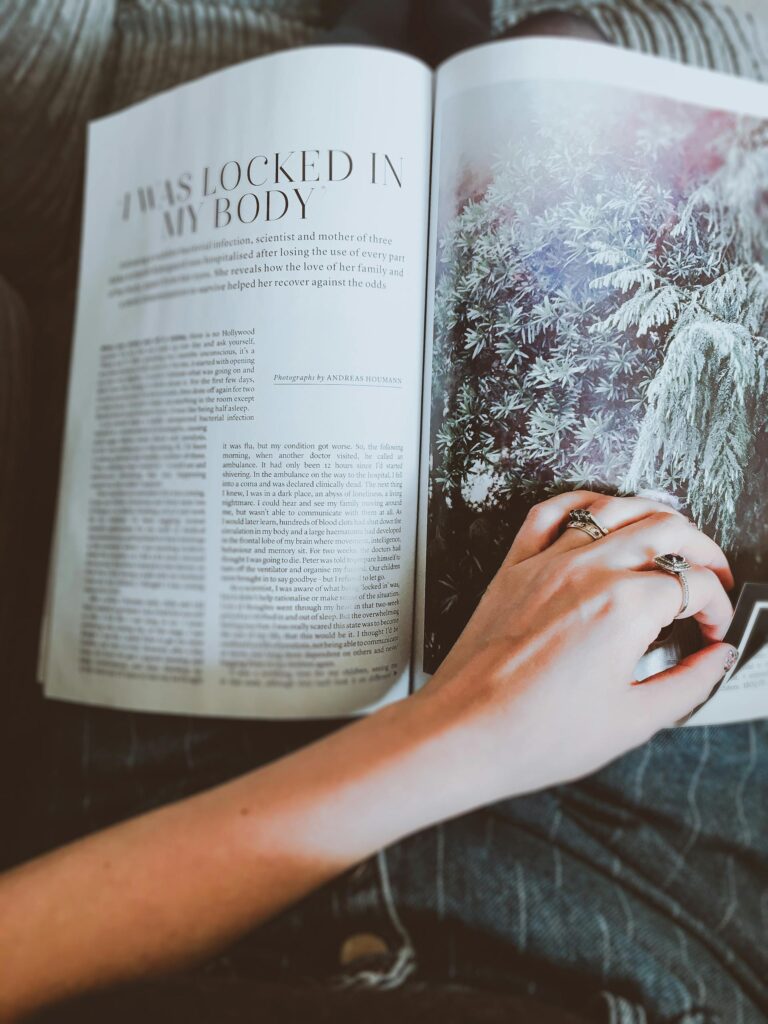 A person leisurely reading a magazine, showcasing a hand with rings on vibrant pages.